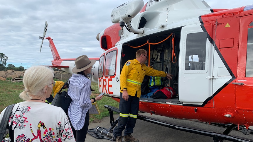 a man standing next to a helicopter with to women