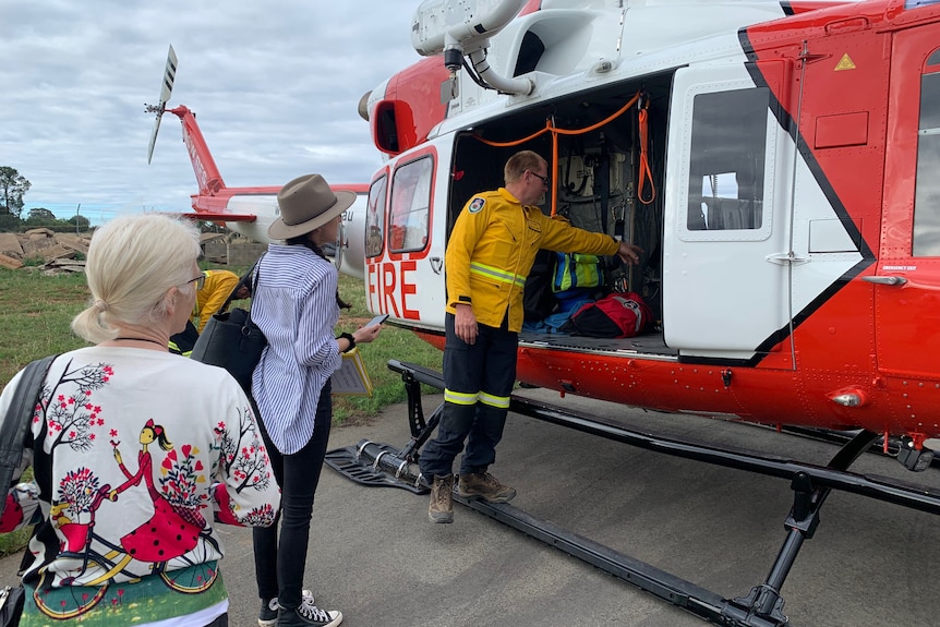 a man standing next to a helicopter with to women