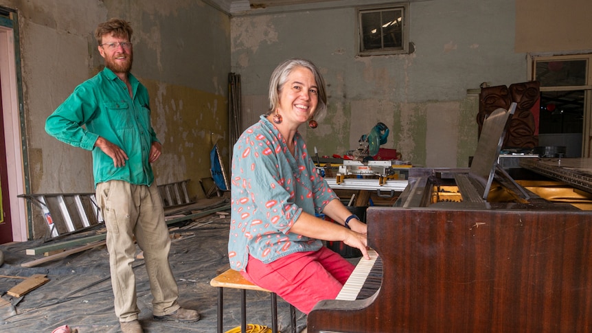Chris and Nerida Cuddy standing next to a piano in building renovation site.