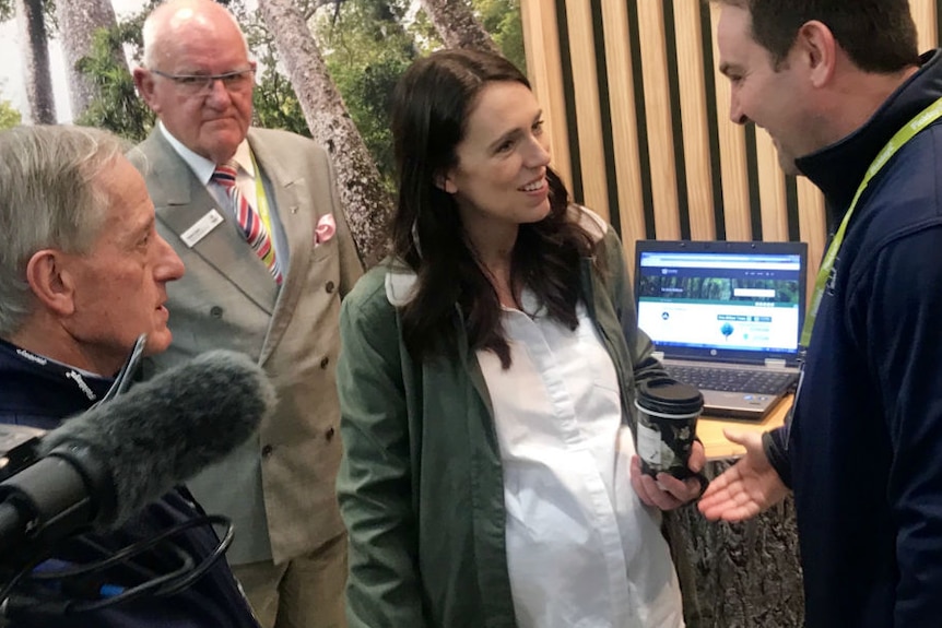 A pregnant Jacinda Arden holds a coffee and talks at an agriculture event.