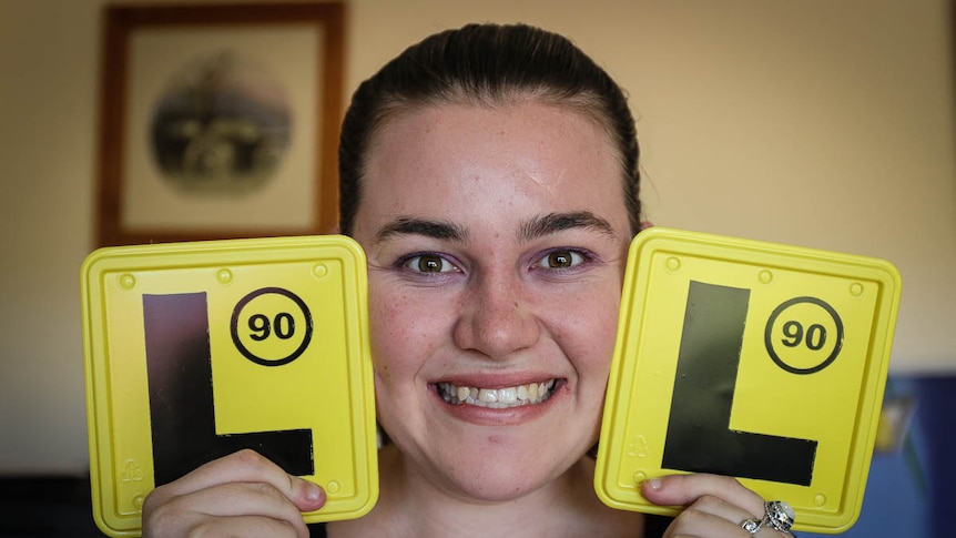 Elizabeth Caughey smiling and holding two L plates next to her face
