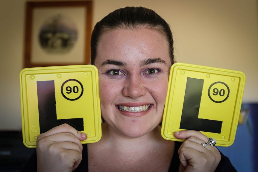 Elizabeth Caughey smiling and holding two L plates next to her face