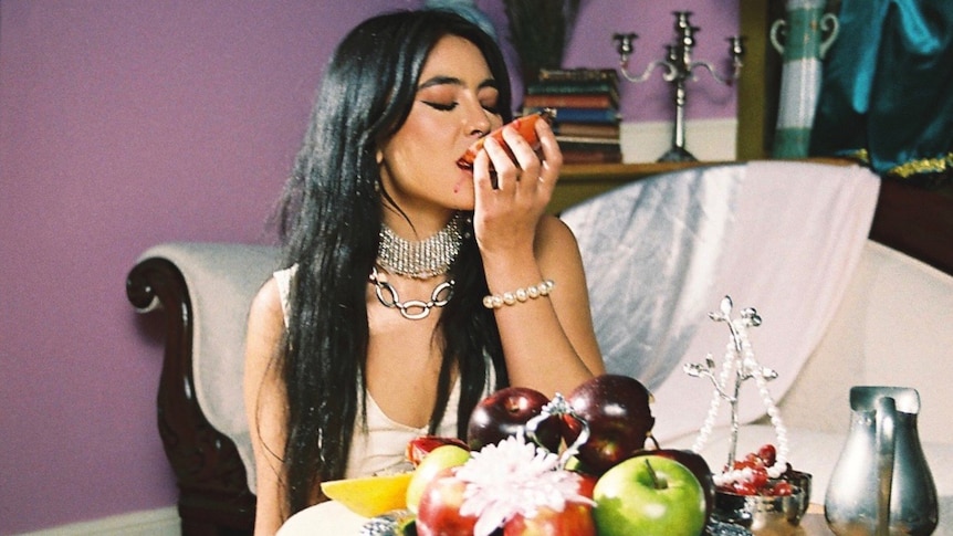 LADY KING lying beside a table with a platter of fruit and biting into a piece of fruit