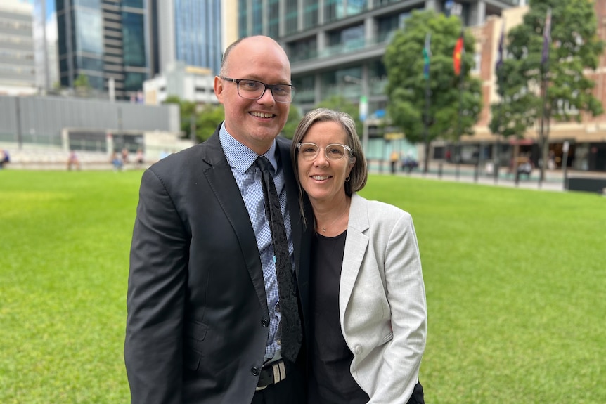 A smiling couple dressed up for court on the lawns outside th Queensland Supreme Court. 
