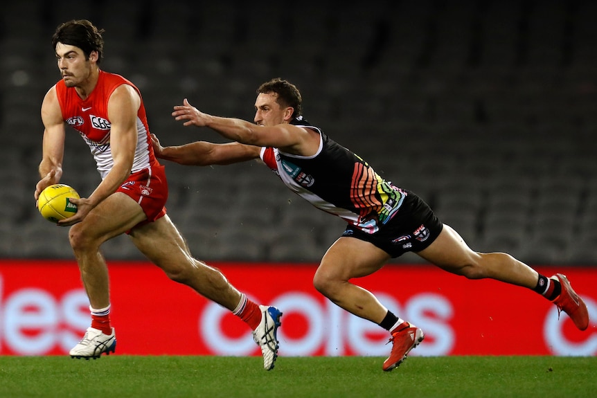 AFL player running the ball with a defender diving to tackle him during a match