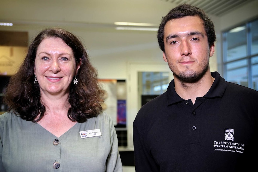 A woman and a man stand side by side in a high school classroom posing for a photo.