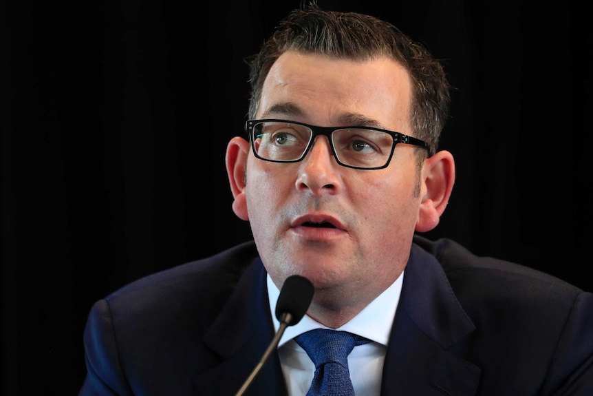 Daniel Andrews sits in front of a microphone.