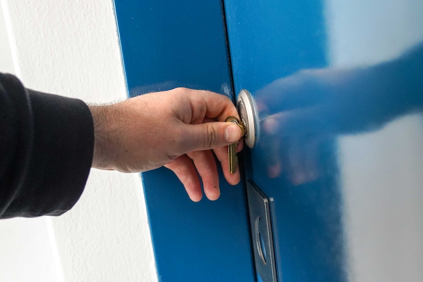 A man's hand turns a key in a blue door, in an apartment building in Sydney.