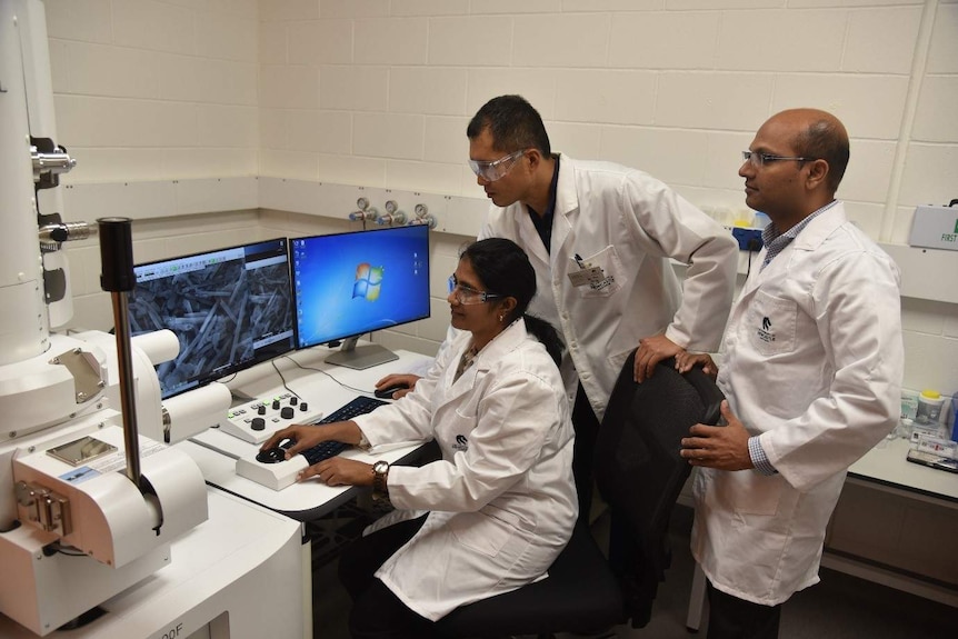 A team of researchers in white lab coats gather around a computer to look at microscope images of the kaolin.