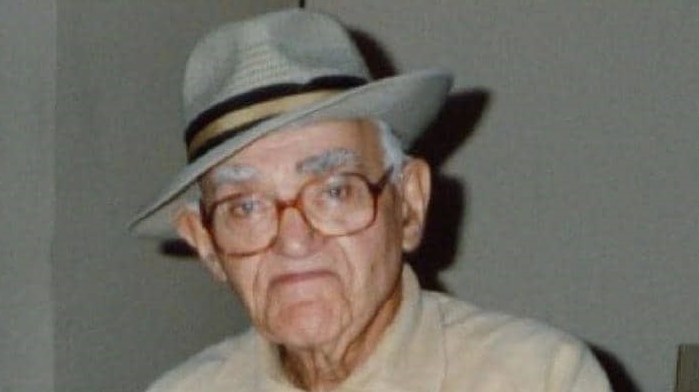 An elderly man, wearing glasses and a grey hat