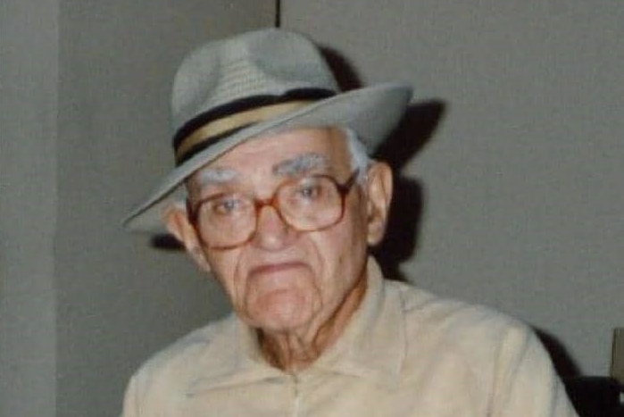 An elderly man, wearing glasses and a grey hat