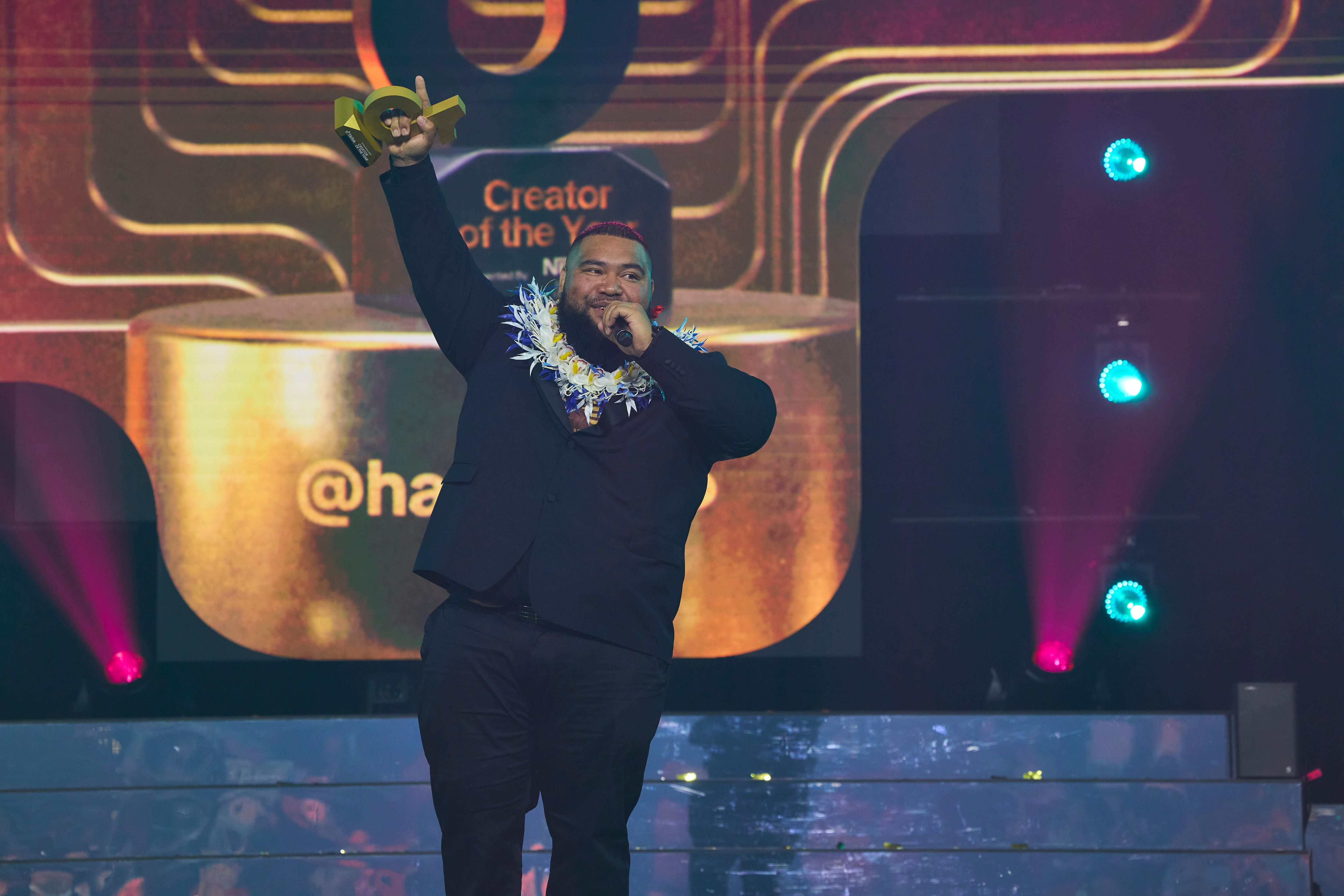 Content creator Havea 676 stands on stage holding award. 
