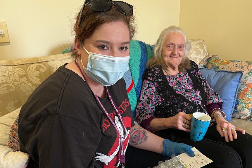 Jessica wearing a blue surgical mask and sitting on the couch with Valerie, who is smiling and holding a mug.