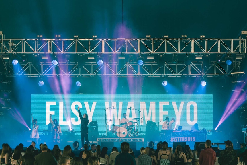 Elsy Wameyo dressed in black and standing on a stage with her arm in the air in front of a crowd