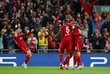 A Liverpool footballer stands with fists outstretched in celebration as he faces three teammates after a goal for his team.