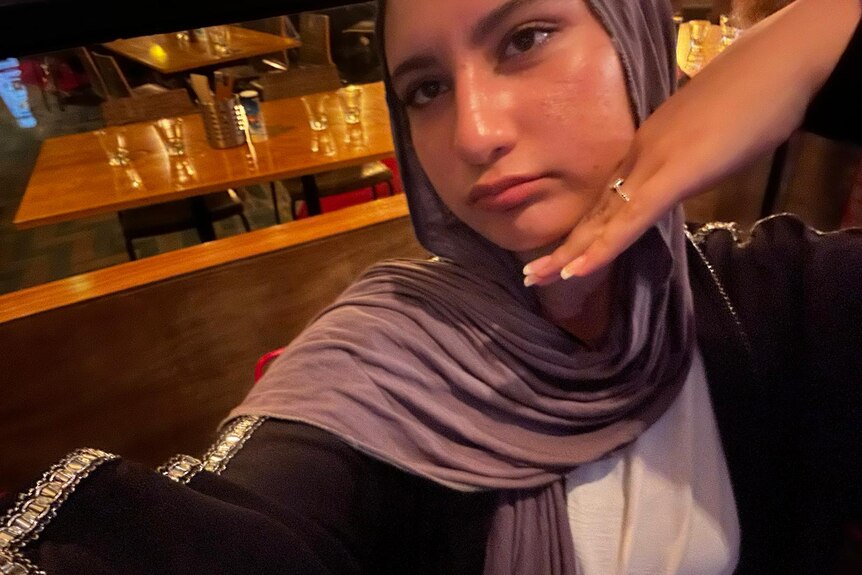 A yound girl in a headscarf poses for a selfie with her hand resting under her chin. 