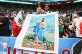 A smiling couple hold a big banner depicting a barefoot Lionel Messi holding a staff with a halo above his head. 