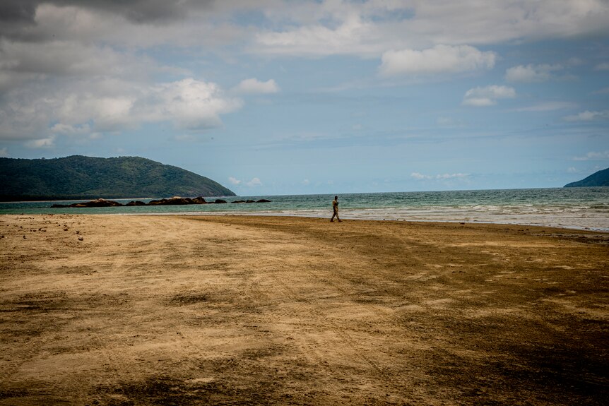 A man alone walking on a beach.