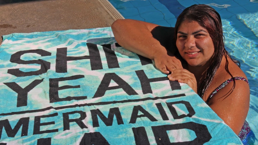 Georgia Pipilairidis hangs on to the side of the pool, she is wearing a mermaid tail.