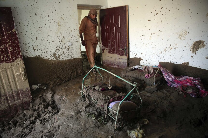 An Afghan man looks for belongings in his house filled with mud. What looks like a child's crib is buried in the sludge.