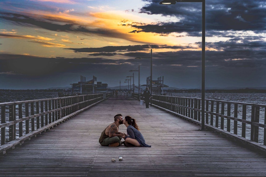 An unknown couple sitting down, kissing on Woody Point Jetty