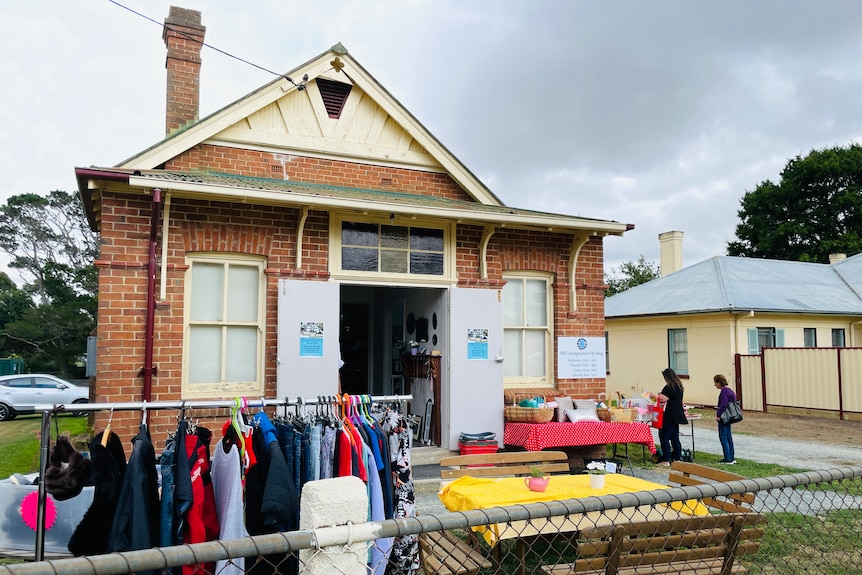 A small building with open doors and racks of clothing outside.