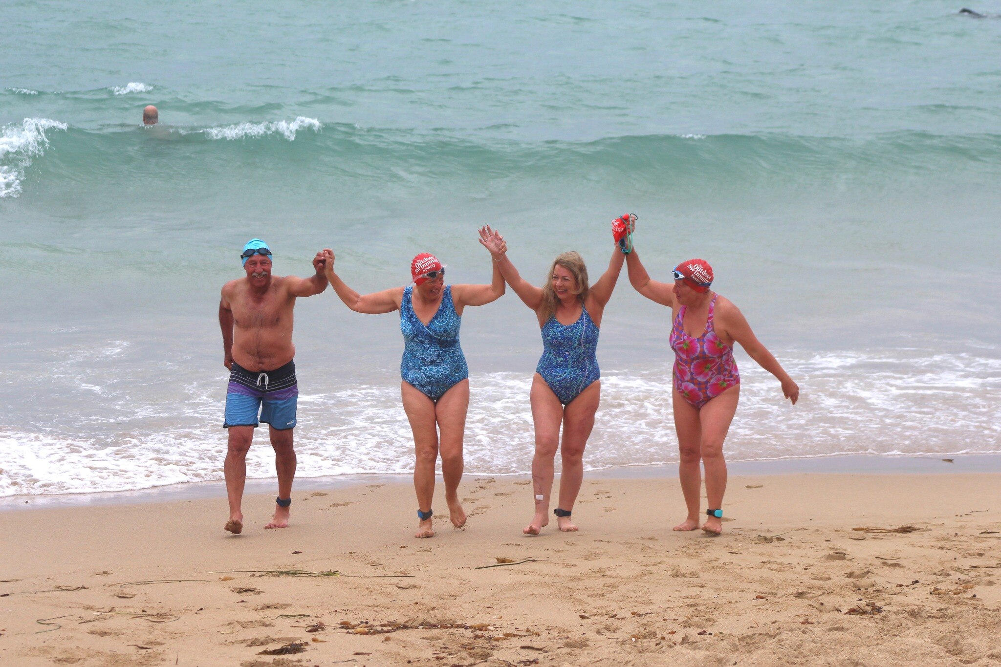 Four swimmers coming out of the water with their arms raised