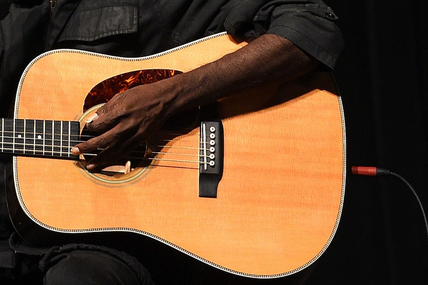 A close up of Australia's most prominent indigenous musician, Dr G Yunupingu, strumming a guitar.