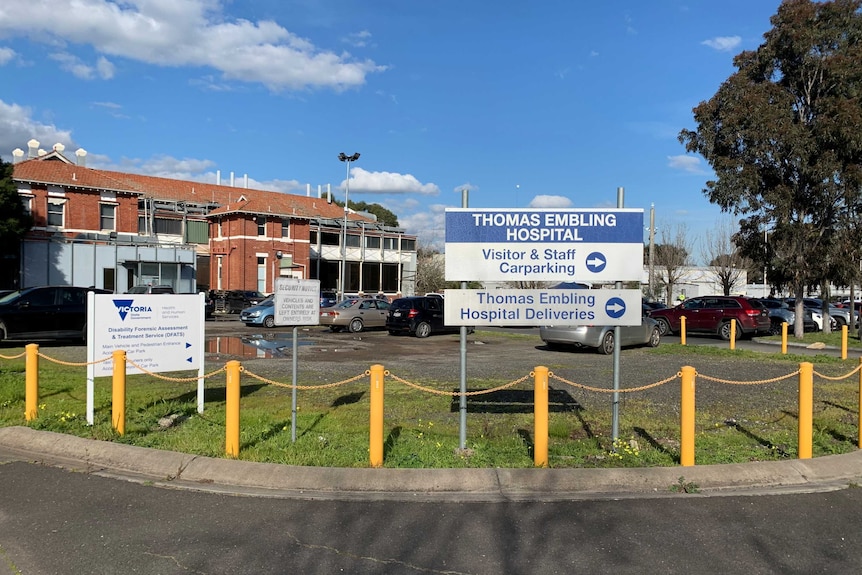 An exterior of a brick hospital building with signs pointing to a car park.