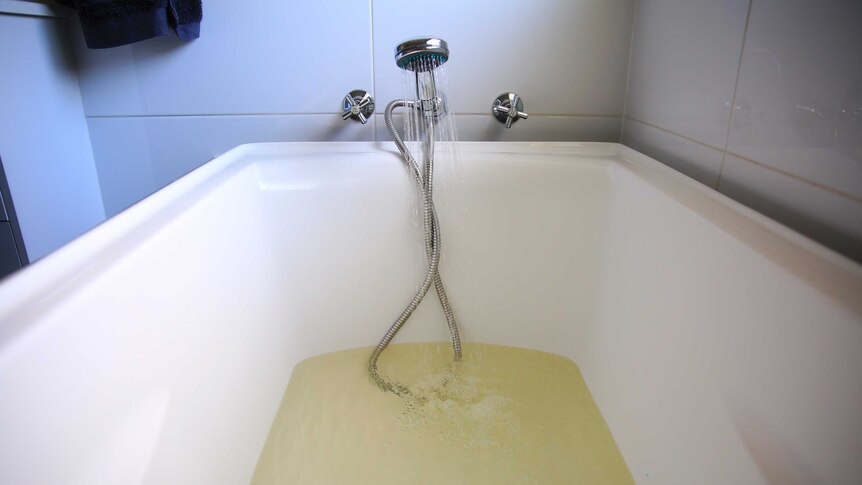 Discoloured, yellow water pours from the tap into a bath.