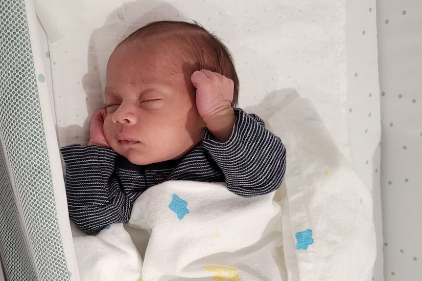 A tiny baby boy in his cot, sleeping