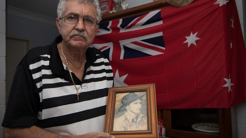 Man stands in front of Red Flag with portrait of soldier father