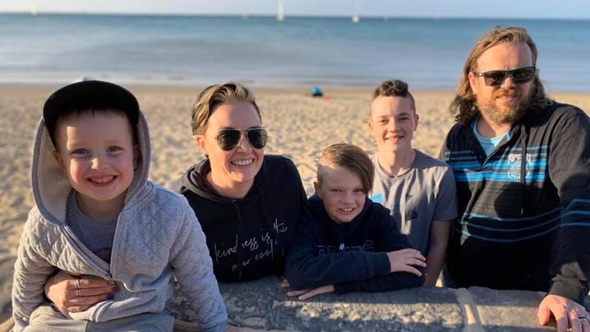 A family of five smiles at the beach.