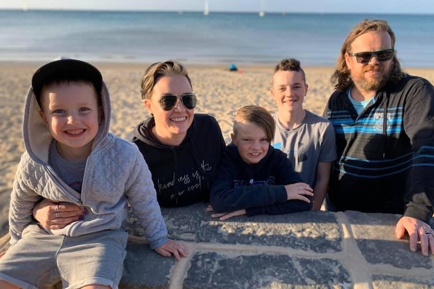 A family of five smiles at the beach.