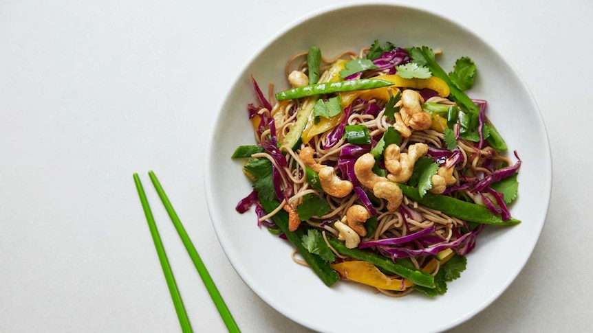 A bowl of soba noodles tossed with chopped snowpeas, cabbage, capsicum and topped with cashews, a quick vegetarian dinner.