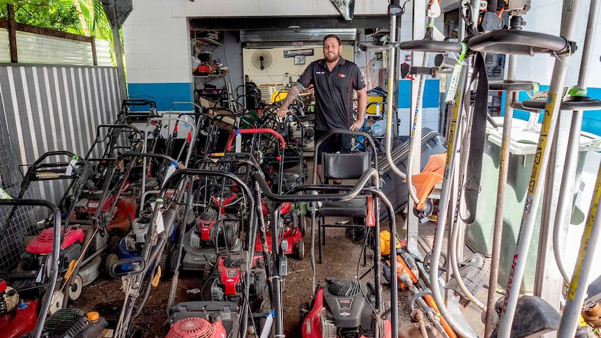 Man stands with a large line of mowers.