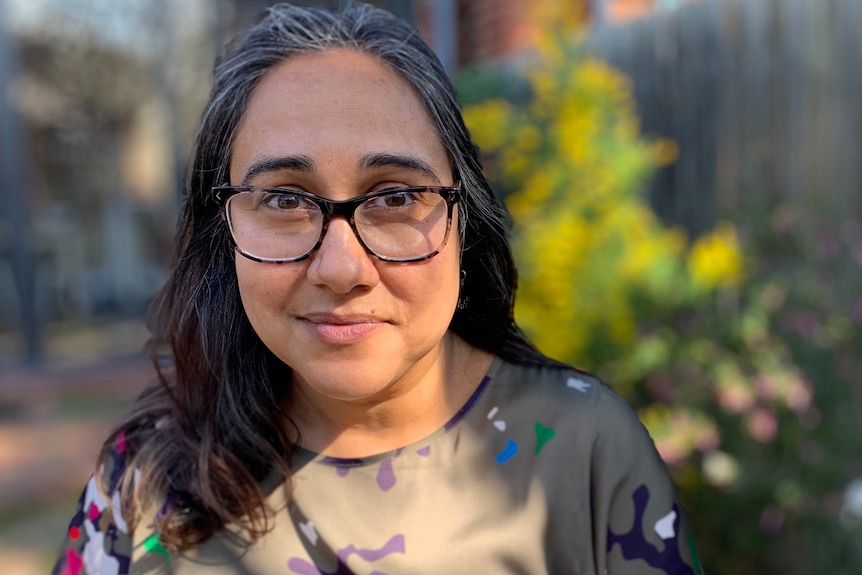 Meena Singh wearing a khaki shirt and glasses, smiling in a photo taken outdoors.