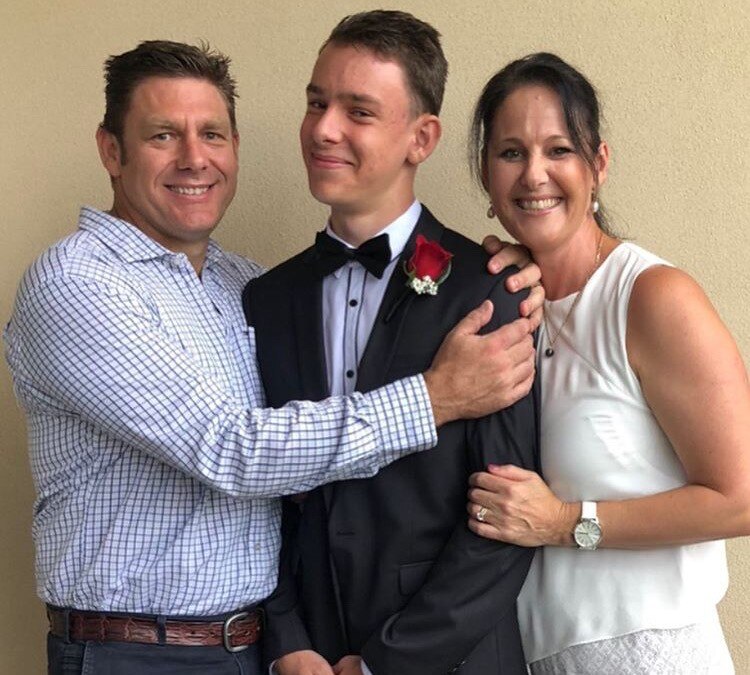 A family: Dad with his arm around his teenage son, who wears a tuxedo, Mum on the right hand side with a big smile. 