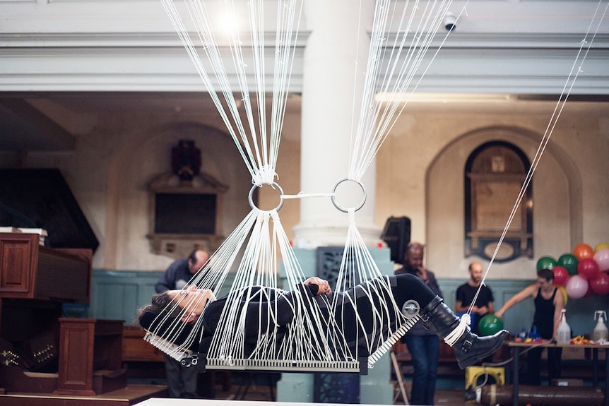 Colour photograph of artist Noëmi Lakmaier bound in ropes to a platform in her artwork Cherophobia.