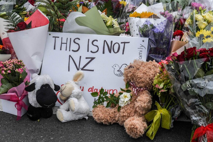 在基督城植物园外为基督城枪击案受害者献上的鲜花中写着“这不是新西兰人”的标语