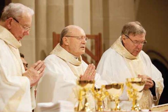 Adrian Doyle, Julian Porteous and George Pell where priest's robes and stand at an altar in prayer