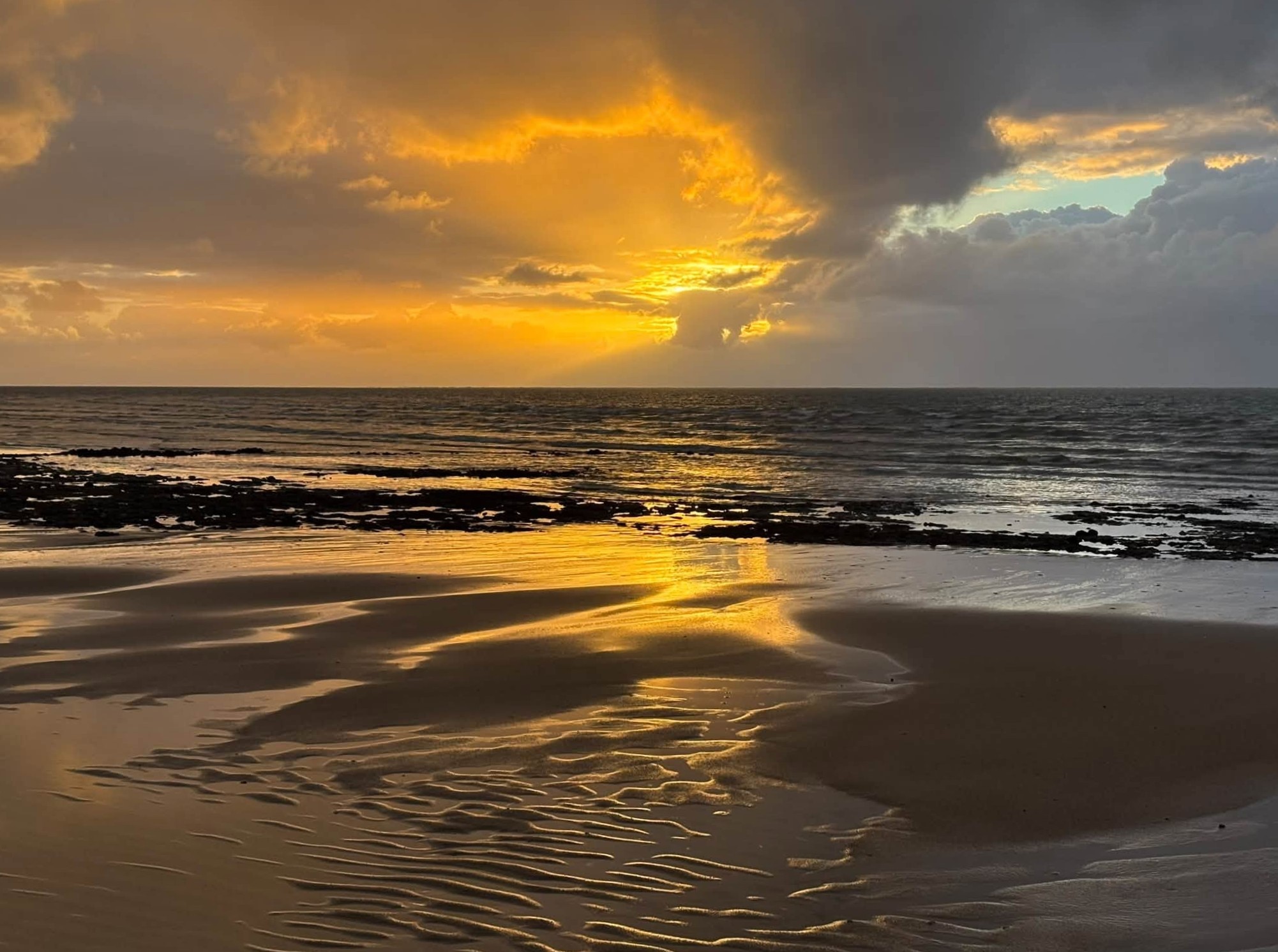 A bright orange sunrise at a rainy beach.