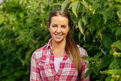 A woman with brown hair, wearing red and white flannelette shirt, standing in front of a tree