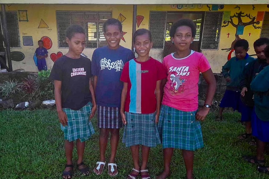Four Fijian students wearing t-shirts and uniform skirts at their school. 