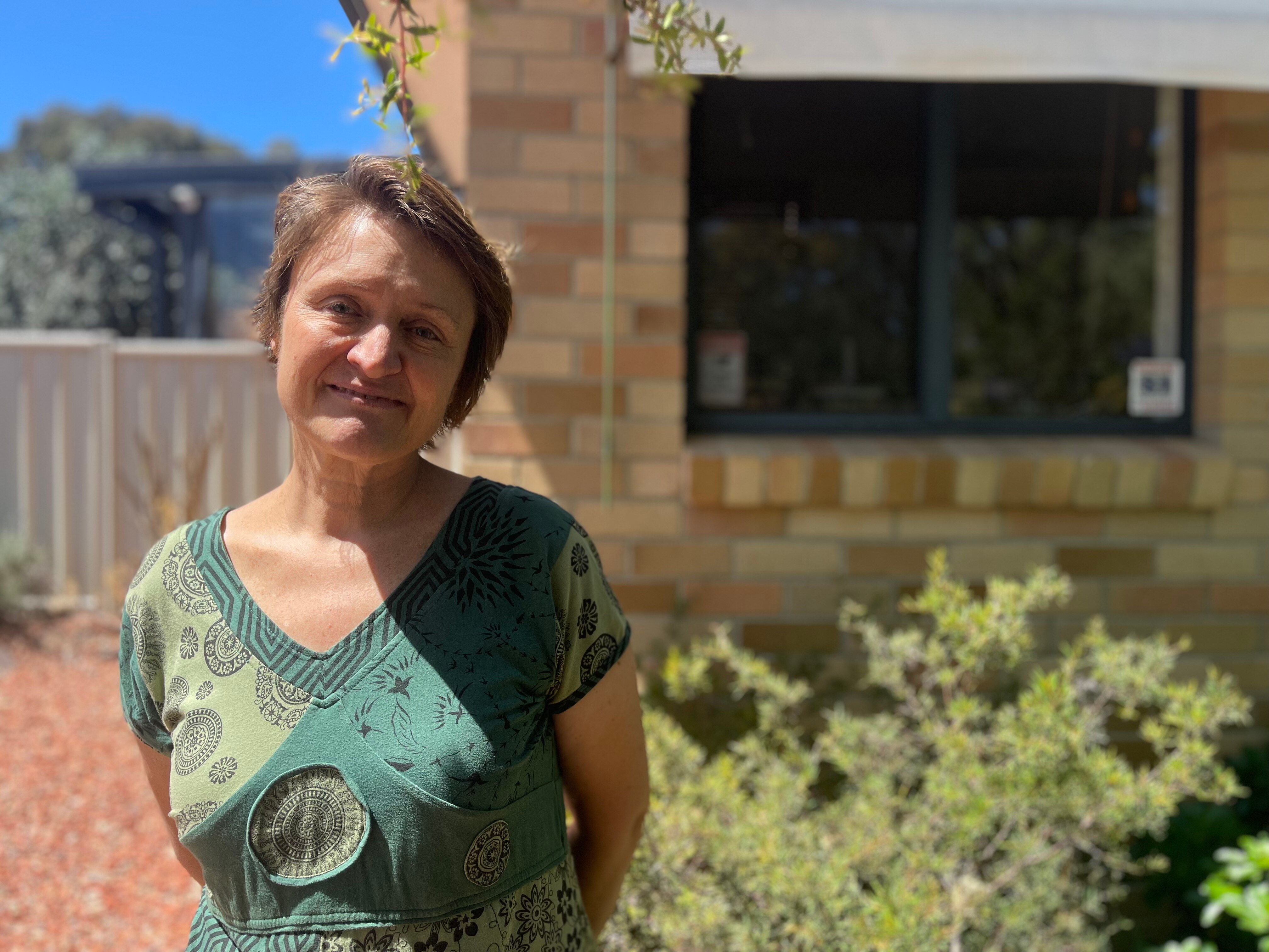 A woman in a green blouse in front of a brick home.