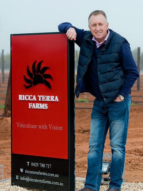 Ashley standing next to a red sign that says ricca terra farms