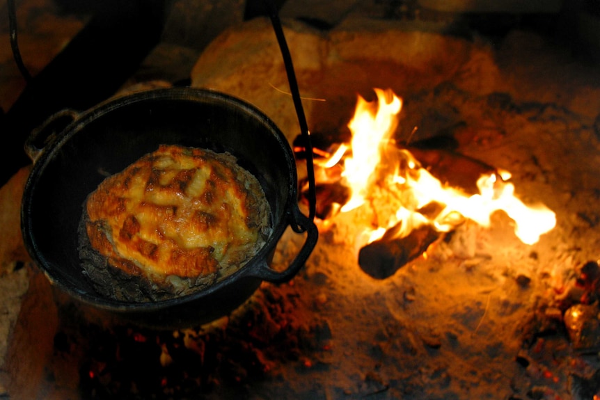 A cast iron pot with damper near a campfire.