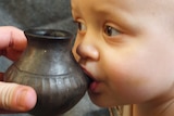 A small infant boy is drinking from a spouted vessel