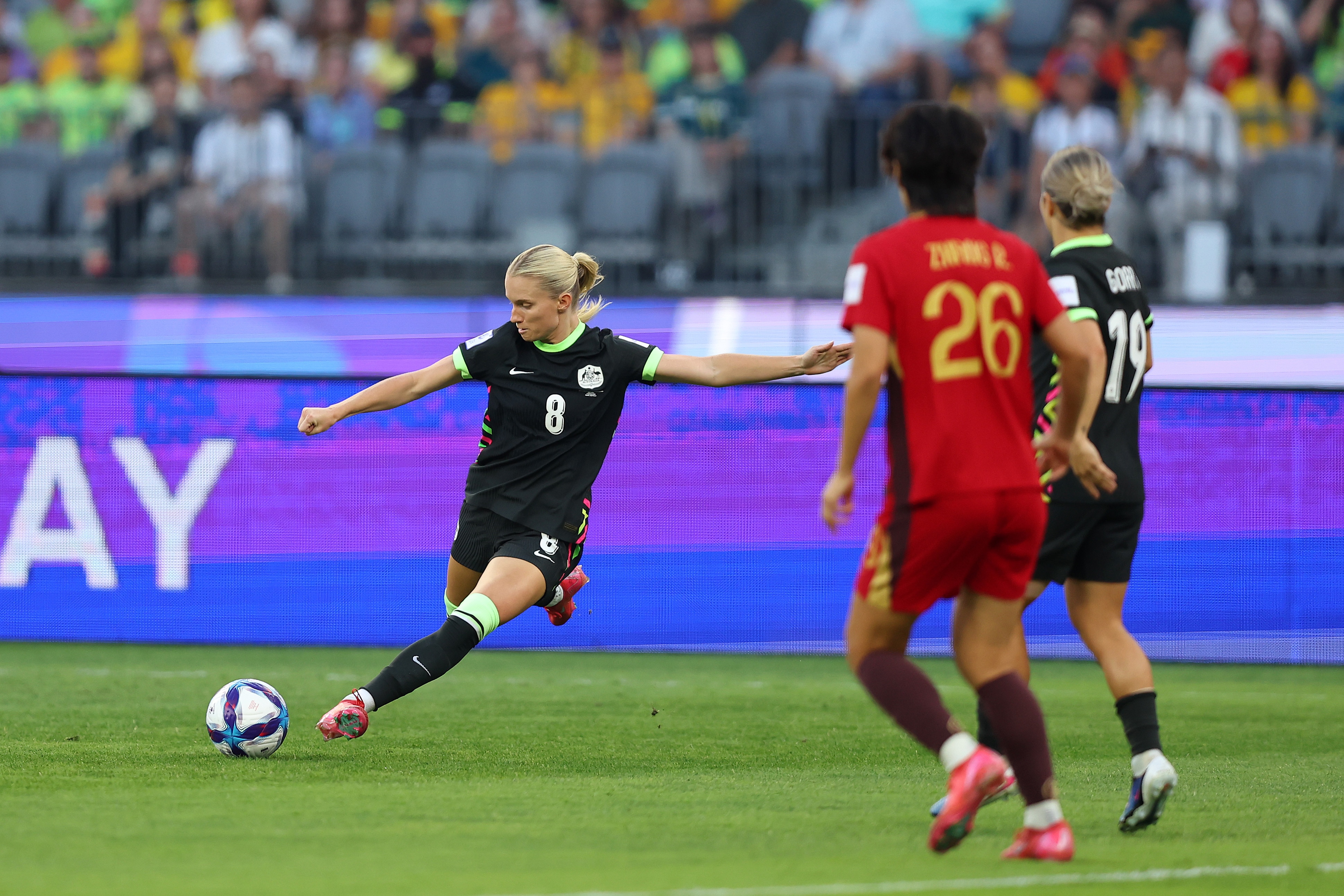 Uma jogadora de futebol de azul escuro cruza a bola com jogadores de vermelho na frente dela