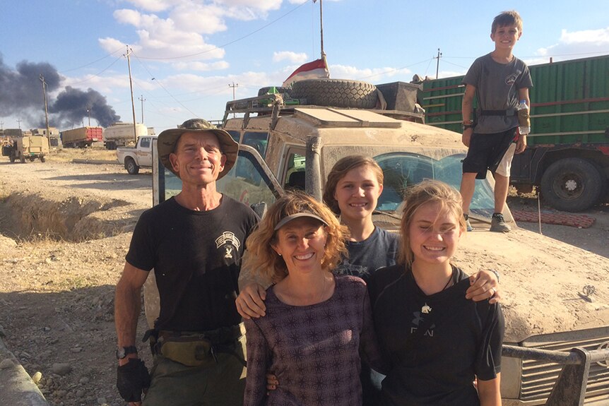 Dave and Karen Eubank and their three kids smile in front of a dusty Humvee, with his son standing on the vehicle's bonnet
